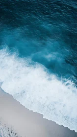 Ocean waves break onto light sand shoreline from above