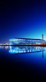 Nighttime panoramic view of blue-lit waterfront arena reflection.
