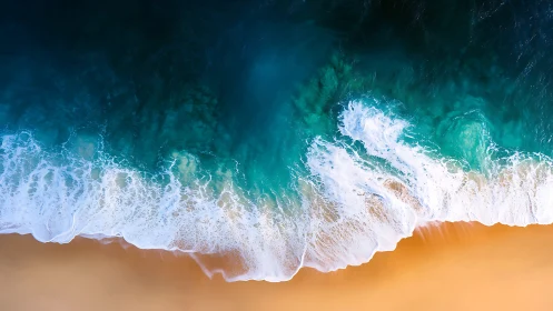 Overhead shoreline with teal waves meeting sand beach.