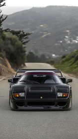 Black sports car sits on winding mountain road in daylight