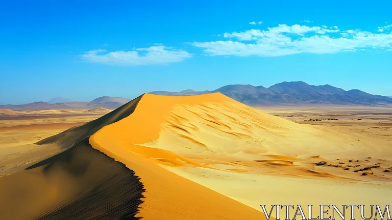 Crested desert sand dune under clear blue sky with mountains
