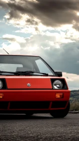 Red vintage hatchback front view under dramatic clouds.