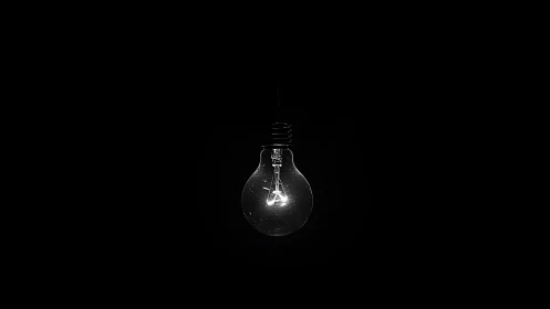 Quiet single lightbulb glows softly in deep darkness