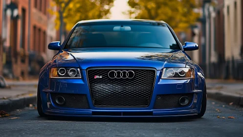 Blue performance sedan front profile on urban autumn street.