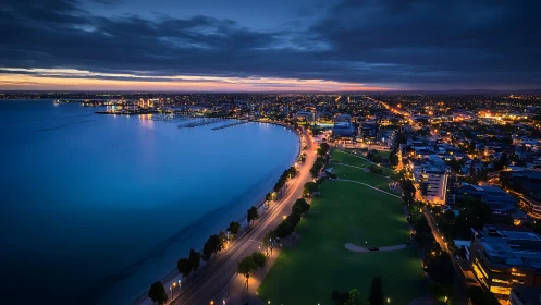 Curved coastal road borders illuminated urban shoreline at dusk