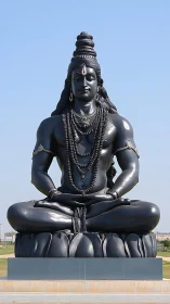 Serene black Shiva statue resting beneath open blue sky.