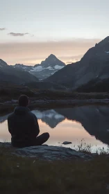 Solitary figure observes alpine peak mirrored in dusk lake