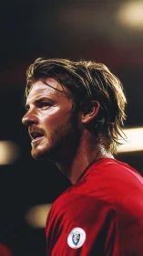 Male football player in red jersey under stadium lights.