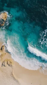 Aerial turquoise surf rolling onto golden sand shoreline.