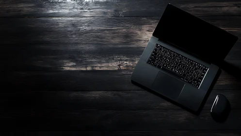 Open black laptop and mouse sit on dark wooden desk surface