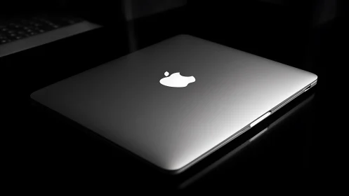 Closed silver laptop with illuminated logo on glossy black.