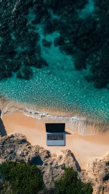 Laptop positioned on sandy beach facing turquoise ocean water
