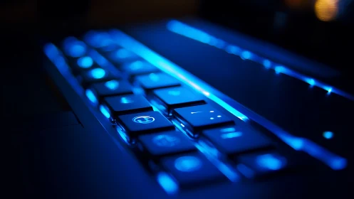 Backlit laptop keyboard in blue low light close focus view.