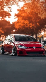 Lowered red hatchback under warm autumn bokeh canopy.