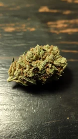 Close-up cannabis bud on distressed black wooden surface.