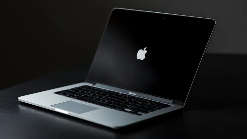 Sleek silver laptop glows softly on dark reflective desk.
