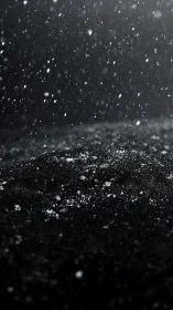 Snowfall drifts across dark textured ground at night.