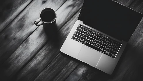 Monochrome laptop workspace on dark wooden desktop.