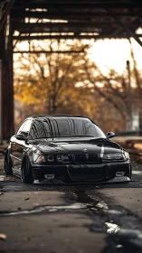 Lowered black BMW sedan under industrial steel structure.