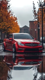 Red Mercedes coupe reflects in autumn rain-soaked street.