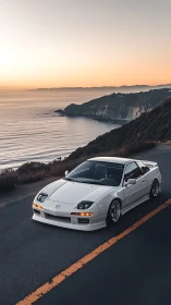 White coupe on coastal highway at dusk near ocean cliffs.
