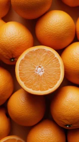 Halved orange rests atop whole oranges in tight overhead view