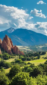 Red rock spires rise before forested mountains and clouds.