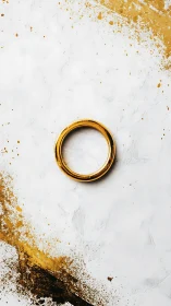 Golden ring rests softly amid bright white and paint splashes
