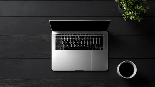 Minimalist silver laptop on dark desk with coffee and plant.