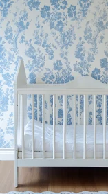 White nursery crib against blue floral toile wallpaper.