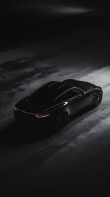 Sleek black sports car parked on dark wet pavement at night.
