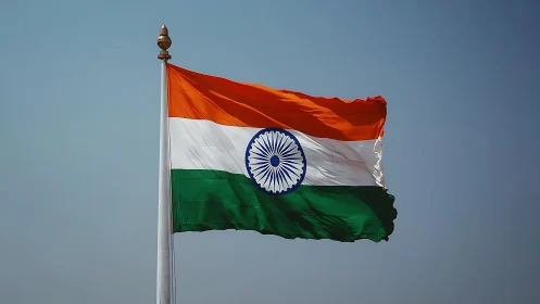 Indian tricolor flag billowing under clear blue sky.