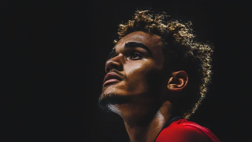 Focused young athlete gazes upward under dramatic spotlight.