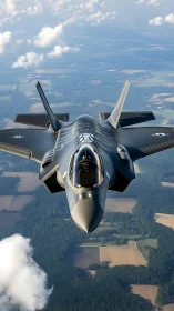 Stealth fighter jet cuts through clouds above patchwork fields.