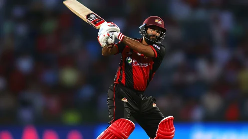 Cricketer in red and black uniform playing attacking shot.