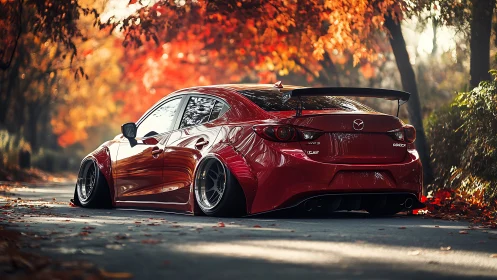 Stanced red Mazda in glowing autumn forest roadway scene.