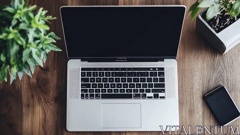 Sleek laptop rests on wooden desk with plants and phone.