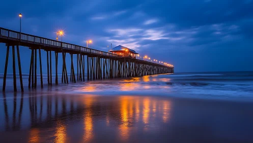 Ocean pier glows over twilight surf with mirrored reflections.