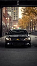 Black Chevrolet sedan centered on urban street under bridge