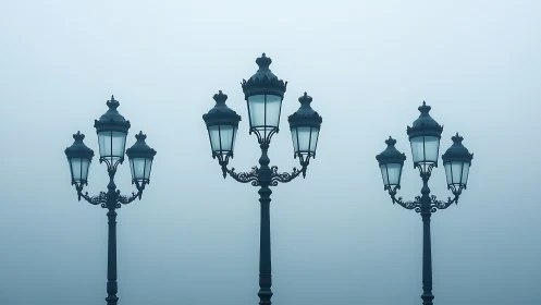 Foggy morning view of three ornate vintage lampposts.