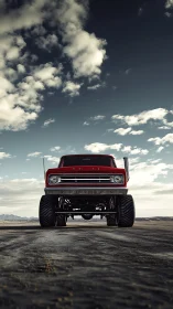 Lifted red truck dominates open desert road beneath clouds
