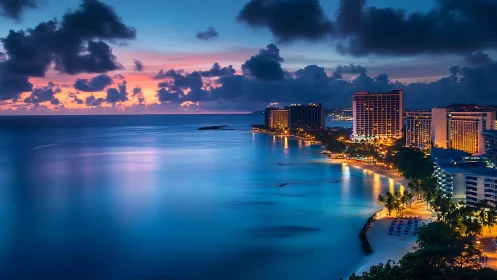 Tropical city shoreline glows under deep blue twilight sky.