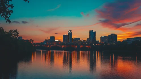 Urban riverfront skyline at dusk with saturated sunset reflections.
