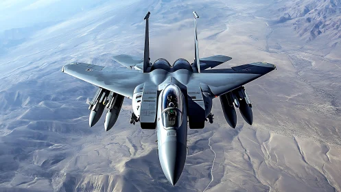 Twin‑engine strike fighter with underwing payload over arid terrain