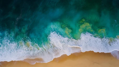 Overhead view of turquoise ocean surf on sandy shoreline.