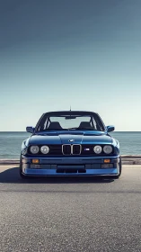 Front view of classic blue BMW M car by coastal roadway.