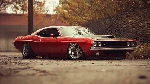 Low-slung red muscle car with black hood in autumn lot.