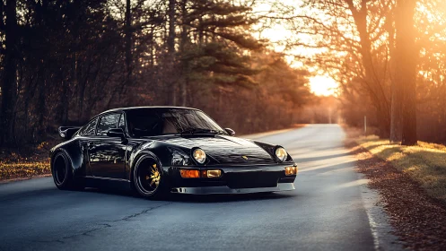 Black widebody sports coupe on empty forest road at sunset