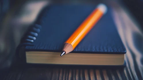 Close-up of orange pencil on closed black notebook.