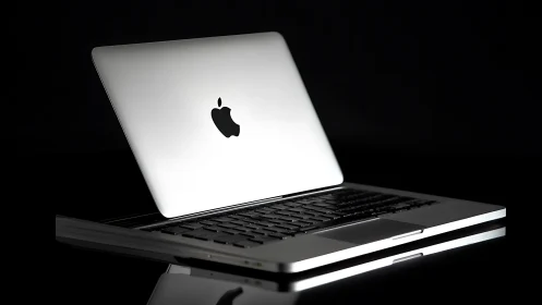 Silver laptop with illuminated logo on reflective surface.